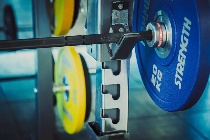 Loaded barbell sitting on rack hooks, with coloured plates stored behind
