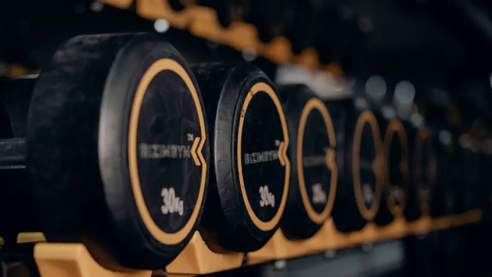 Dark rack of round dumbbells with gold weight numbers