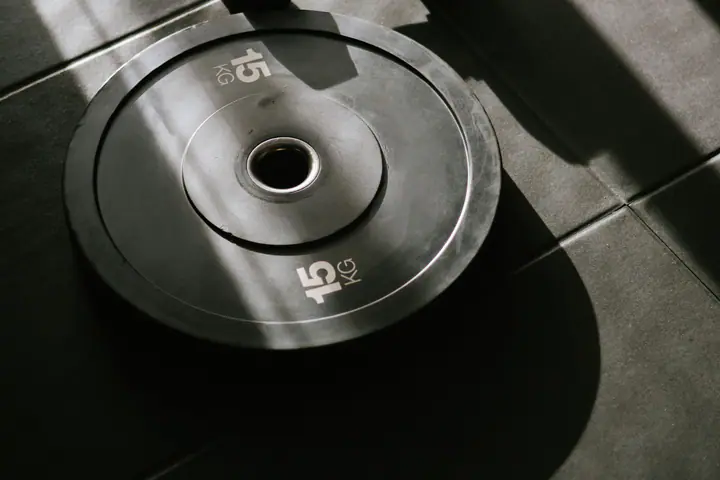 Black-and-white photo of a bumper plate and a dumbbell on a sunlit gym floor