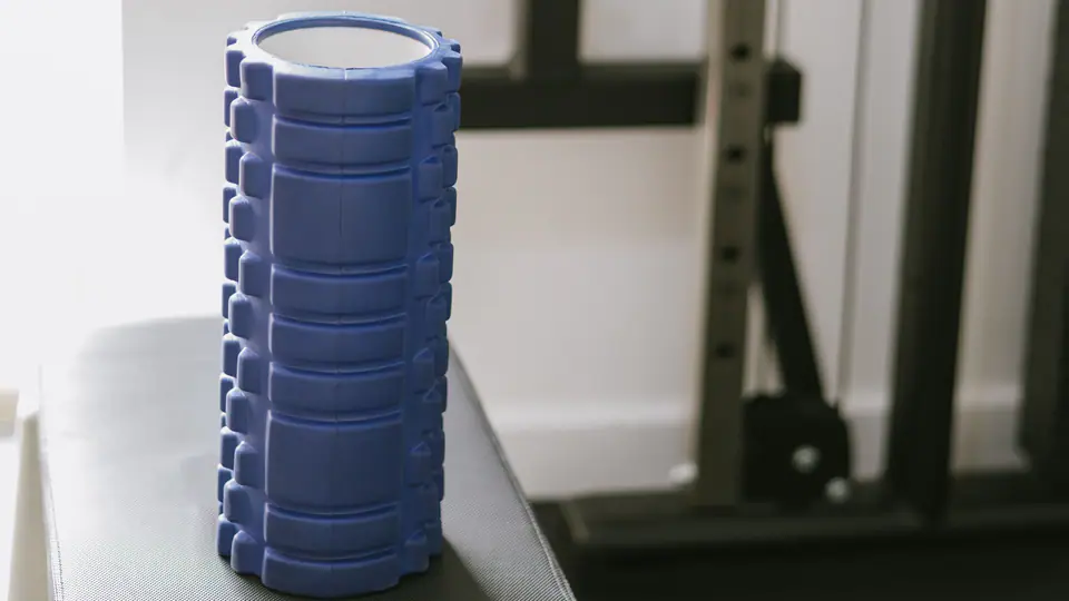 Blue foam roller standing on a plyo box next to a cable machine