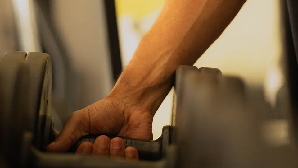 Close-up of a hand wrapping around a dumbbell handle on the rack