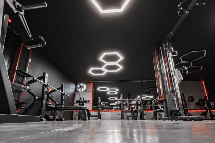 Dark gym with hexagon ceiling lights above rows of strength machines