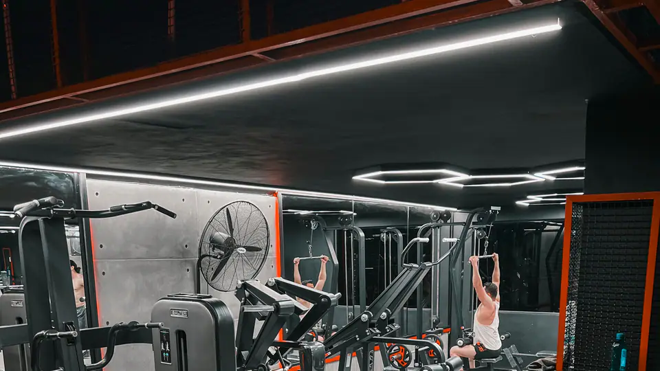 Gym floor with plate-loaded machines, a lat pulldown station and a dumbbell rack