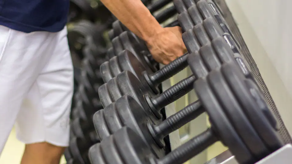 Tattooed lifter taking a heavy dumbbell from the rack