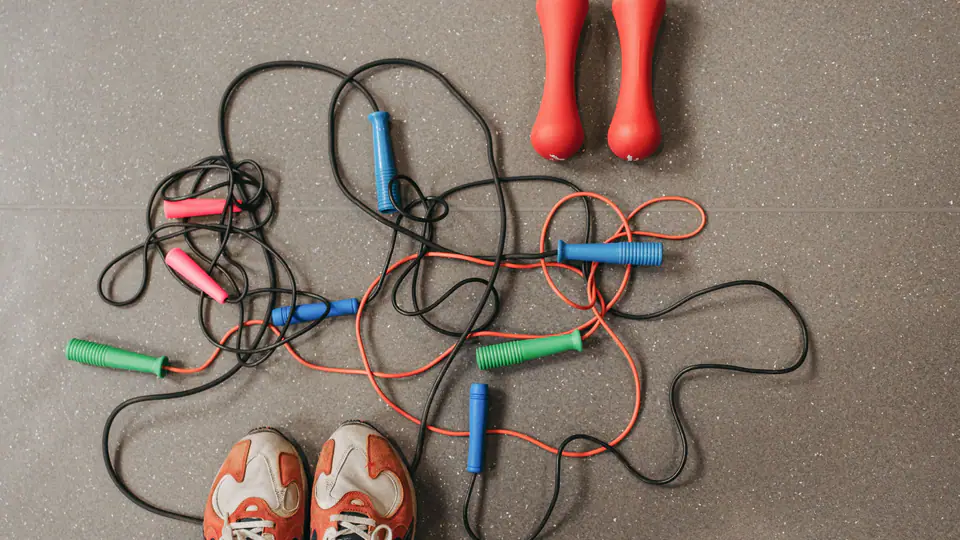 Jump ropes, red dumbbells and a pair of trainers on a gym floor, from above