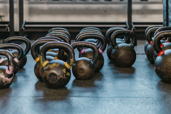 Kettlebells on the floor in front of a dumbbell rack and a large window