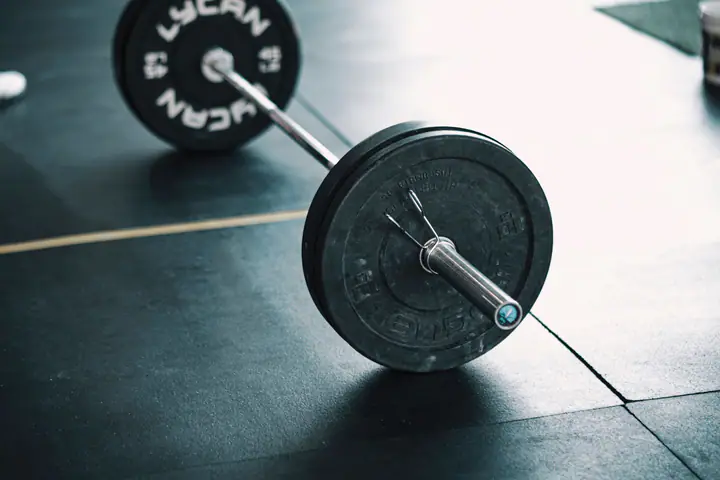 Barbell loaded with bumper plates resting on a gym floor, ready to be deadlifted