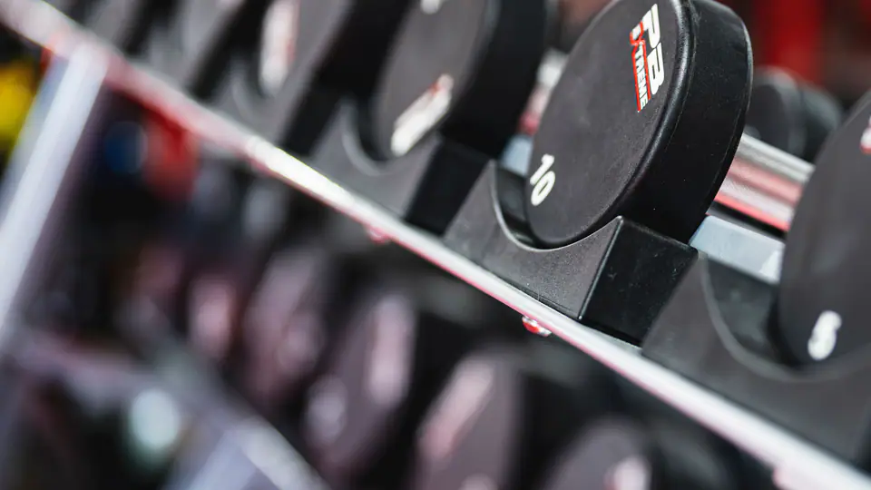 Long rack of round dumbbells in a busy gym, shot at an angle