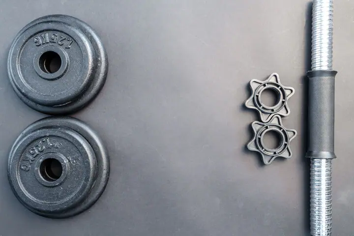 Two small iron plates, spin-lock collars and a dumbbell handle laid out on a grey surface