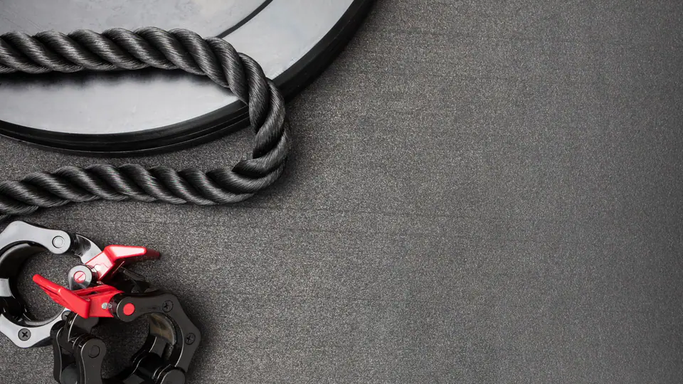 Flat lay of a rubber weight plate, a rope and barbell collars on a gym floor
