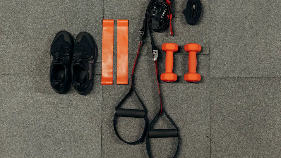 Flat lay of trainers, mini resistance bands, suspension straps and orange dumbbells