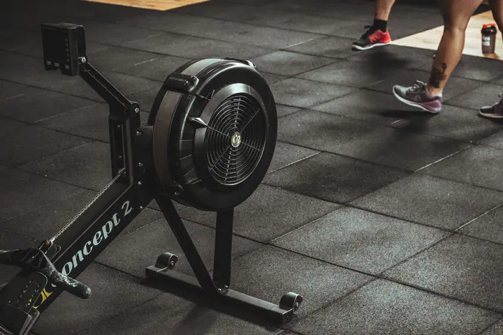 Air rowing machine on a rubber tile gym floor while people walk past