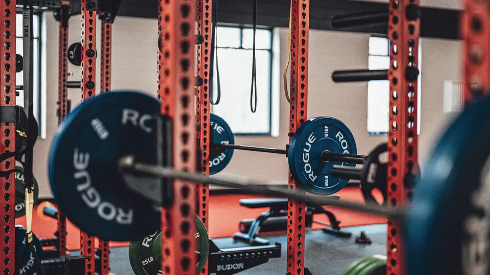 Barbell loaded with bumper plates set in a red power rack