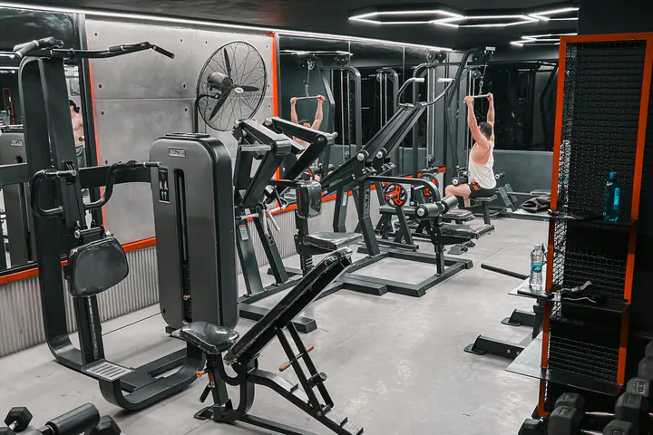 Gym floor with plate-loaded machines, a lat pulldown station and a dumbbell rack