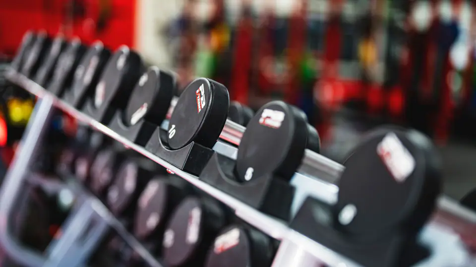 Long rack of round dumbbells in a busy gym, shot at an angle