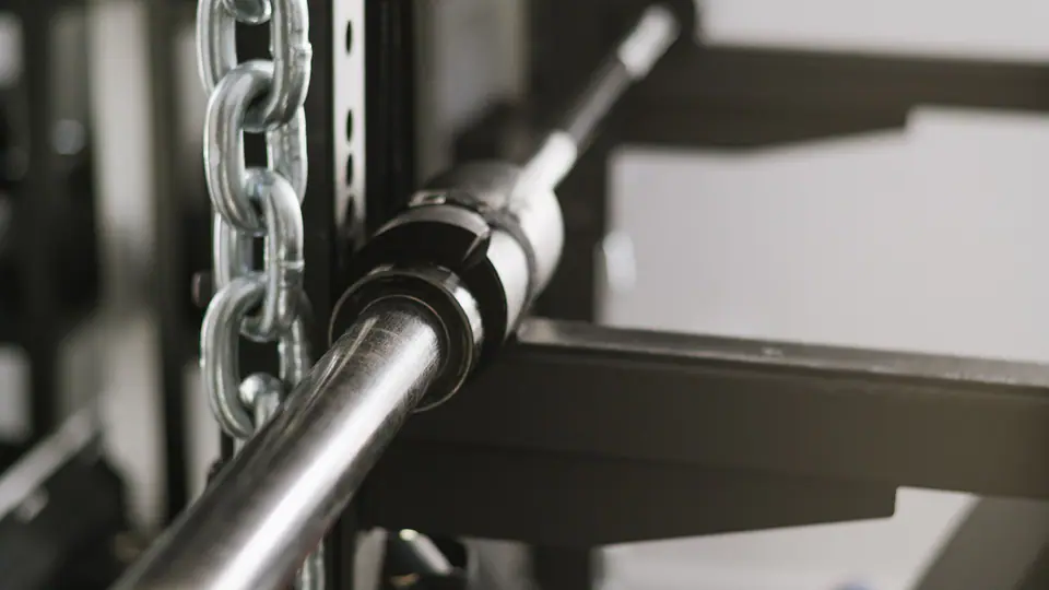 Barbell resting in a rack beside a hanging chain, with a protein shaker on the shelf below