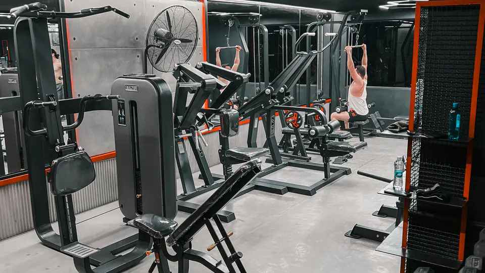 Gym floor with plate-loaded machines, a lat pulldown station and a dumbbell rack